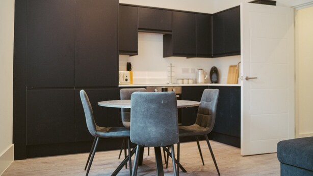 A modern kitchen with dark cabinetry, a round dining table, and four grey chairs. - Apartment 4 (York)
