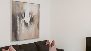 A modern living room with a grey sectional sofa, a large abstract painting, and a flat-screen TV on a white stand. - Apartment 4 (York)