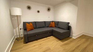 A modern living room with a grey sectional sofa, two orange cushions, a floor lamp, and decorative wall sconces. - Apartment 2 (York)