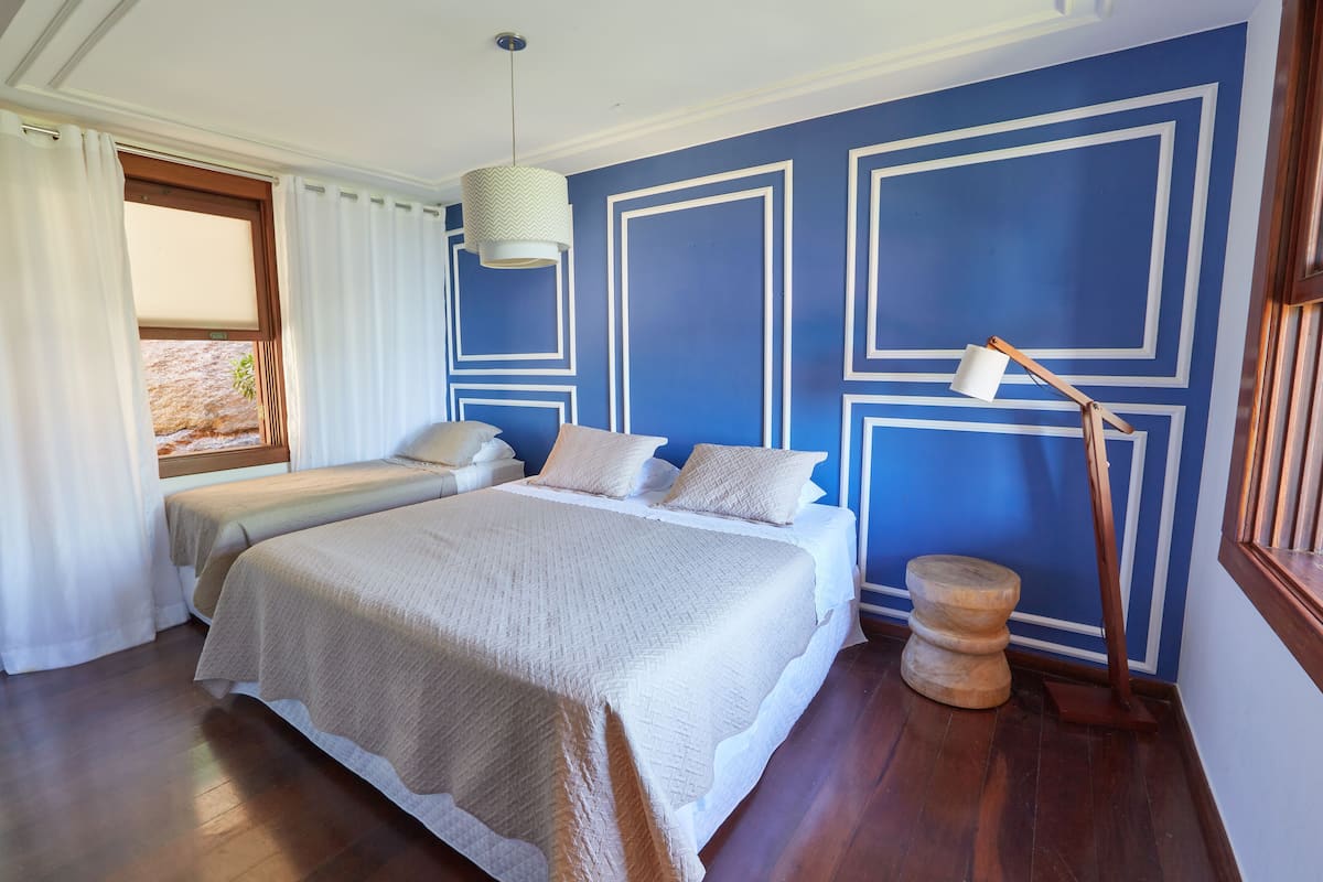 A bedroom with a large bed, two smaller beds, a wooden side table, and a hanging lamp.