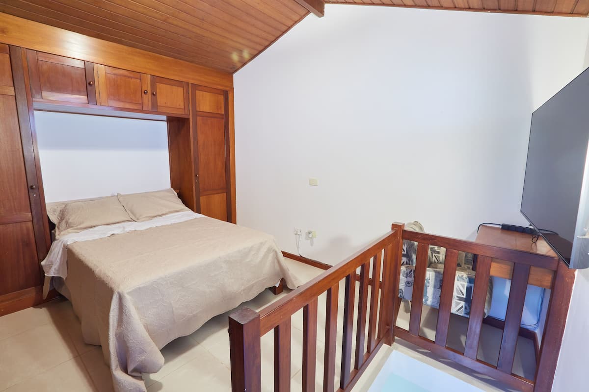 A bedroom with a bed, wooden headboard, and a TV on a stand.