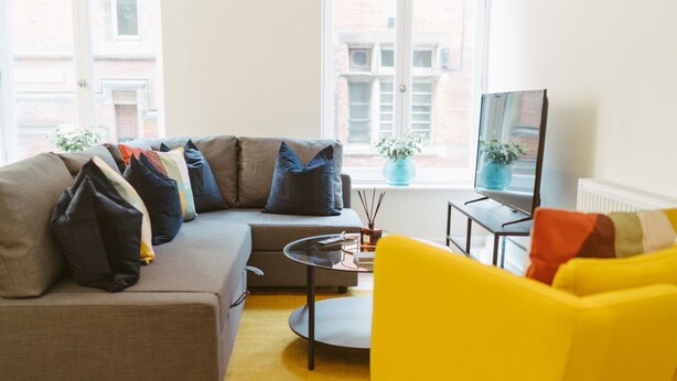 A modern living room with a sofa, yellow armchair, and a TV on a stand. - Apartment 1 (York)