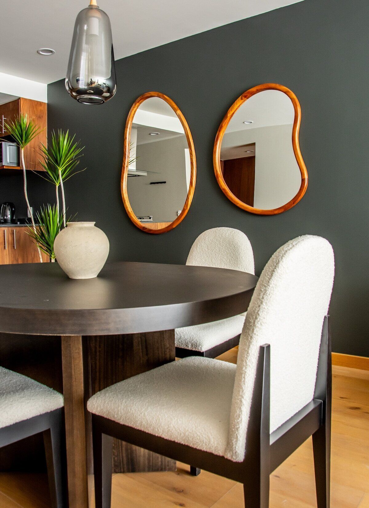 Un coin repas comprenant une table ronde, deux chaises, un vase et deux miroirs fixés au mur.