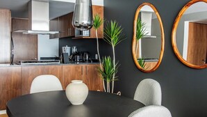 Une cuisine moderne avec des murs sombres, des meubles en bois et une table à manger noire avec des chaises. Deux miroirs ovales sont accrochés au mur, et un luminaire suspendu éclaire l’espace.