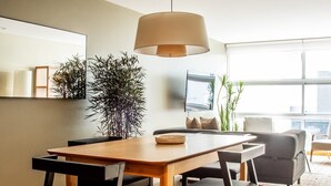 Een moderne eetruimte met een houten tafel en zwarte stoelen, een hanglamp en een groot raam met uitzicht op de stad.