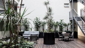 Een terras op het dak met houten vloer, een grijze bank, een eettafel met stoelen en diverse potplanten.