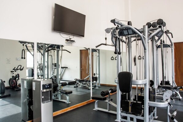 A gym with various exercise machines, a television mounted on the wall, and a mirror reflecting the equipment. - Great location, pool, rooftop, gym, 24/7 security (Ciudad de México)