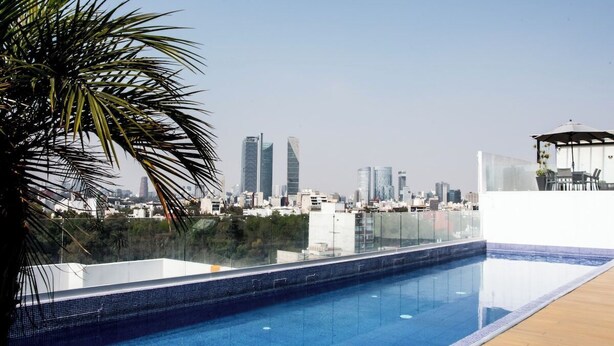 Ein Pool auf dem Dach mit Blick auf eine Stadtlandschaft, umgeben von Palmen und modernen Gebäuden.