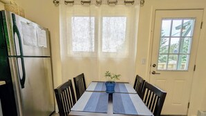 A dining area with a table, chairs, a potted plant, and a refrigerator.