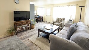 A living room with a television, sofa, coffee table, and a dining area in the background.