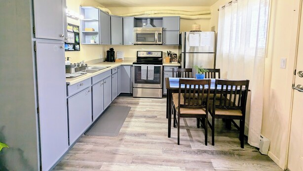 A compact kitchen with grey cabinets, a dining table with chairs, a built-in oven, and a refrigerator.