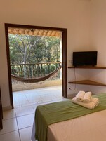 Una habitación con una cama, un televisor sobre una estantería, una hamaca y vistas a árboles a través de una puerta abierta.