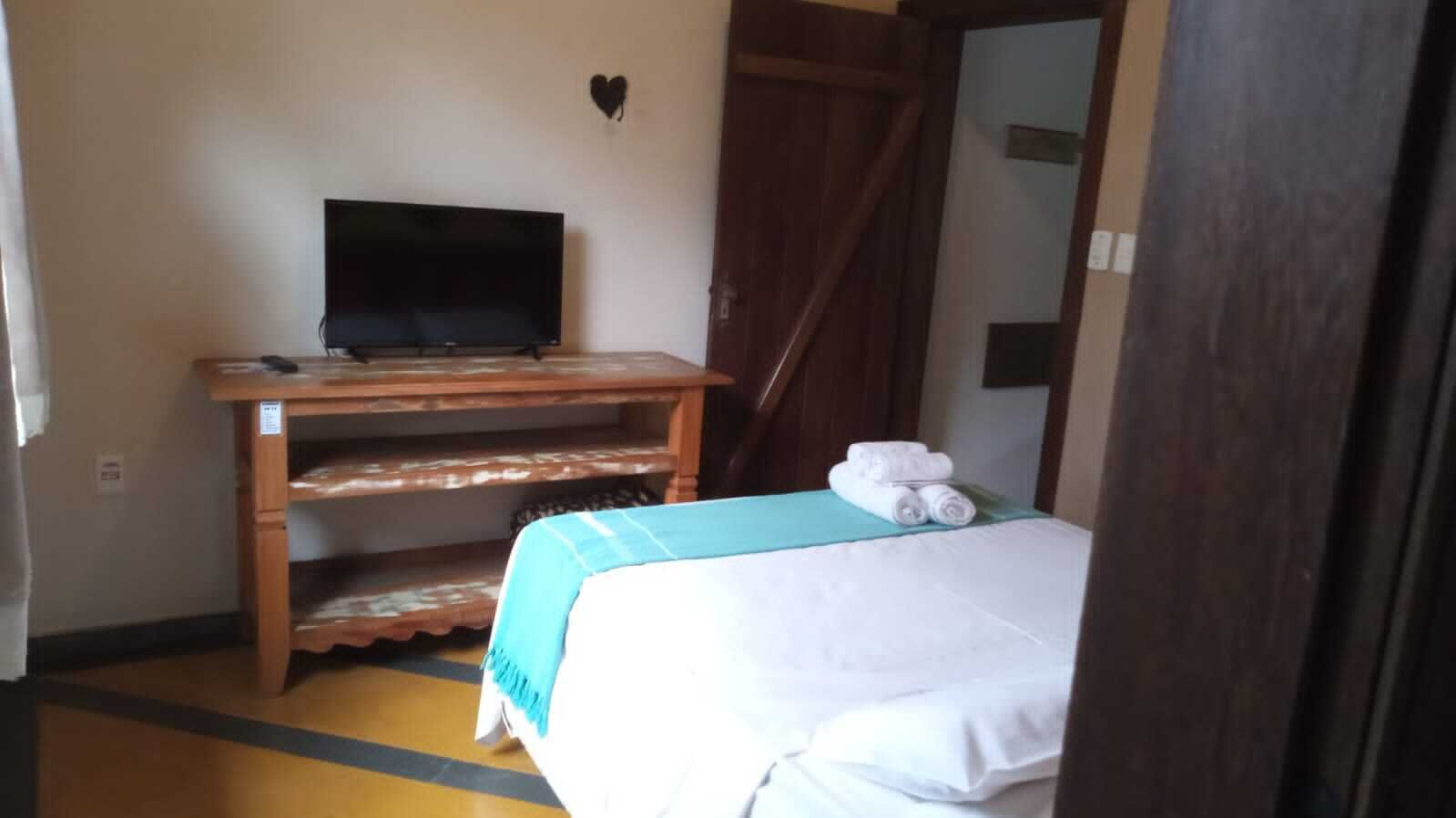 A room with a bed, a TV on a wooden stand, and a heart-shaped decoration on the wall.
