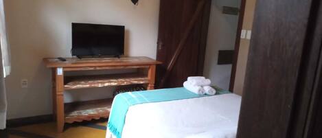 A room with a bed, a TV on a wooden stand, and a heart-shaped decoration on the wall.