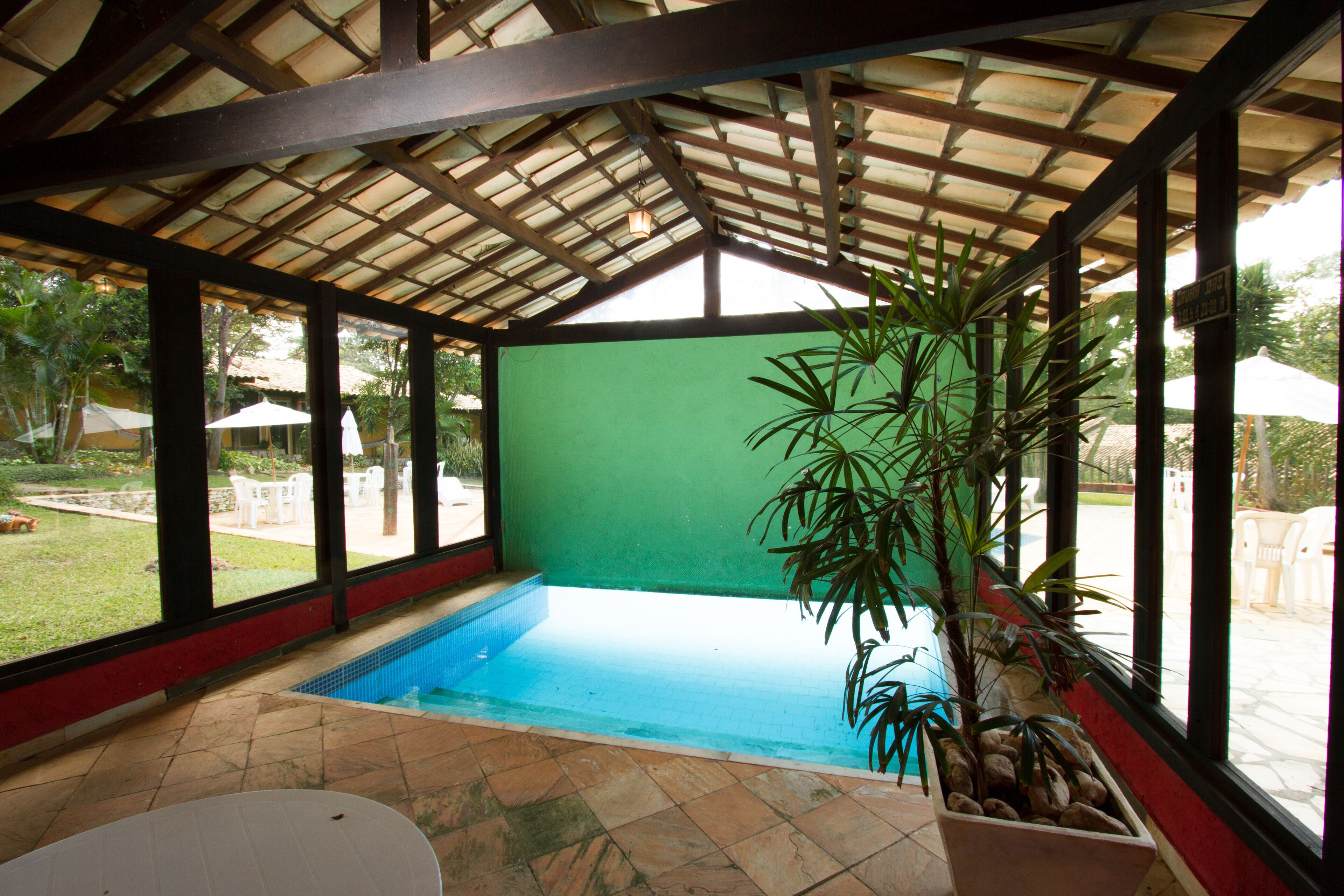 An indoor swimming pool with a tiled floor, surrounded by large windows and a wooden ceiling.