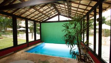 An indoor swimming pool with a tiled floor, surrounded by large windows and a wooden ceiling.