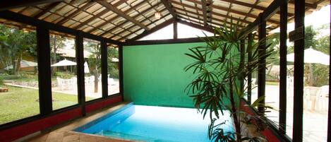 An indoor swimming pool with a tiled floor, surrounded by large windows and a wooden ceiling.