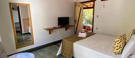 A room with a bed, a small table, a chair, a TV, and a mirror.