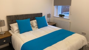 A neatly made bed with a white and blue bedspread, two blue pillows, and a grey headboard. - Apartment 5 (York)