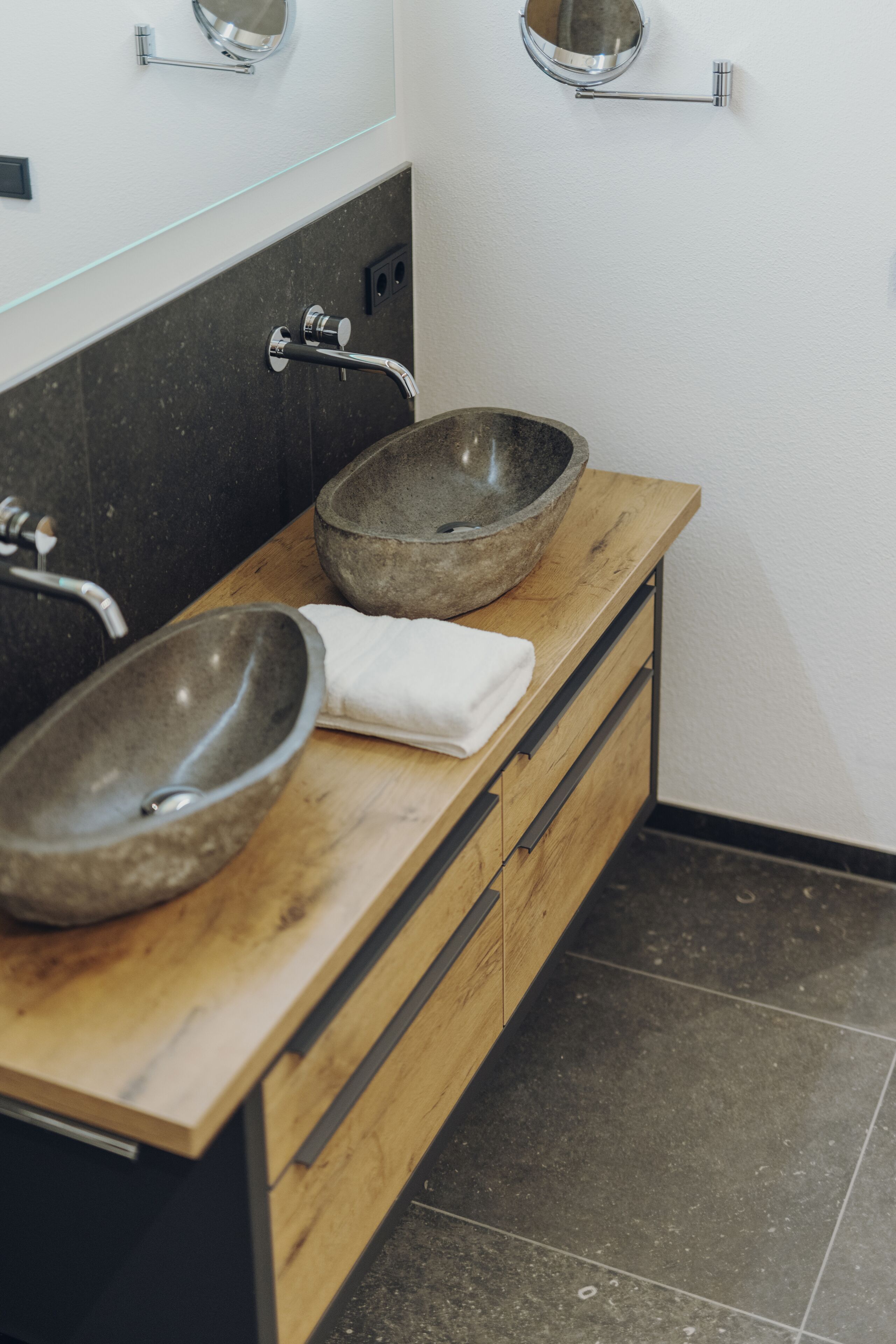 A bathroom with two stone sinks, a wooden vanity, and a towel on the counter.