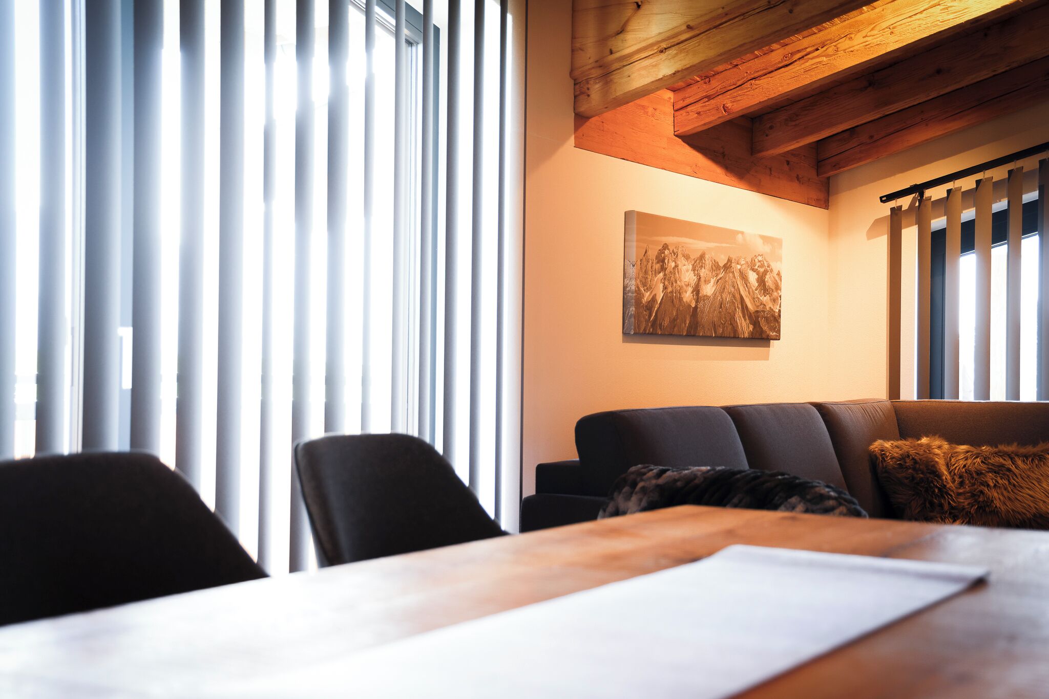 Una sala de estar moderna con techo de madera, un sofá, una mesa de comedor y un ventanal con persianas.