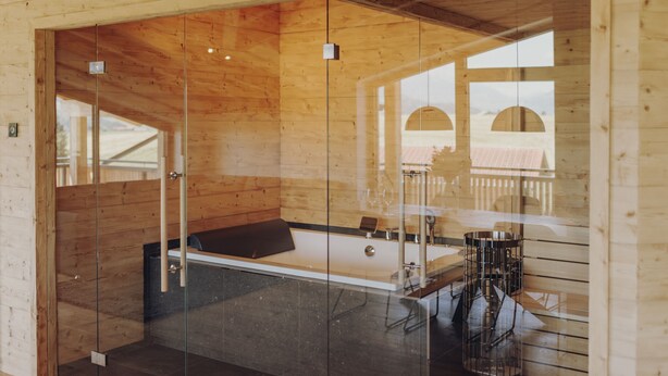 A wooden interior with a glass partition, a bench, and a table. - Platzhirsch First Class Living (Ofterschwang)
