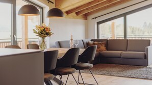 A modern living space with a dining area, a sofa, and large windows. - Platzhirsch First Class Living (Ofterschwang)