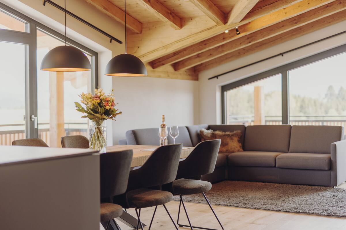 A modern living space with a dining area, a sofa, and large windows.