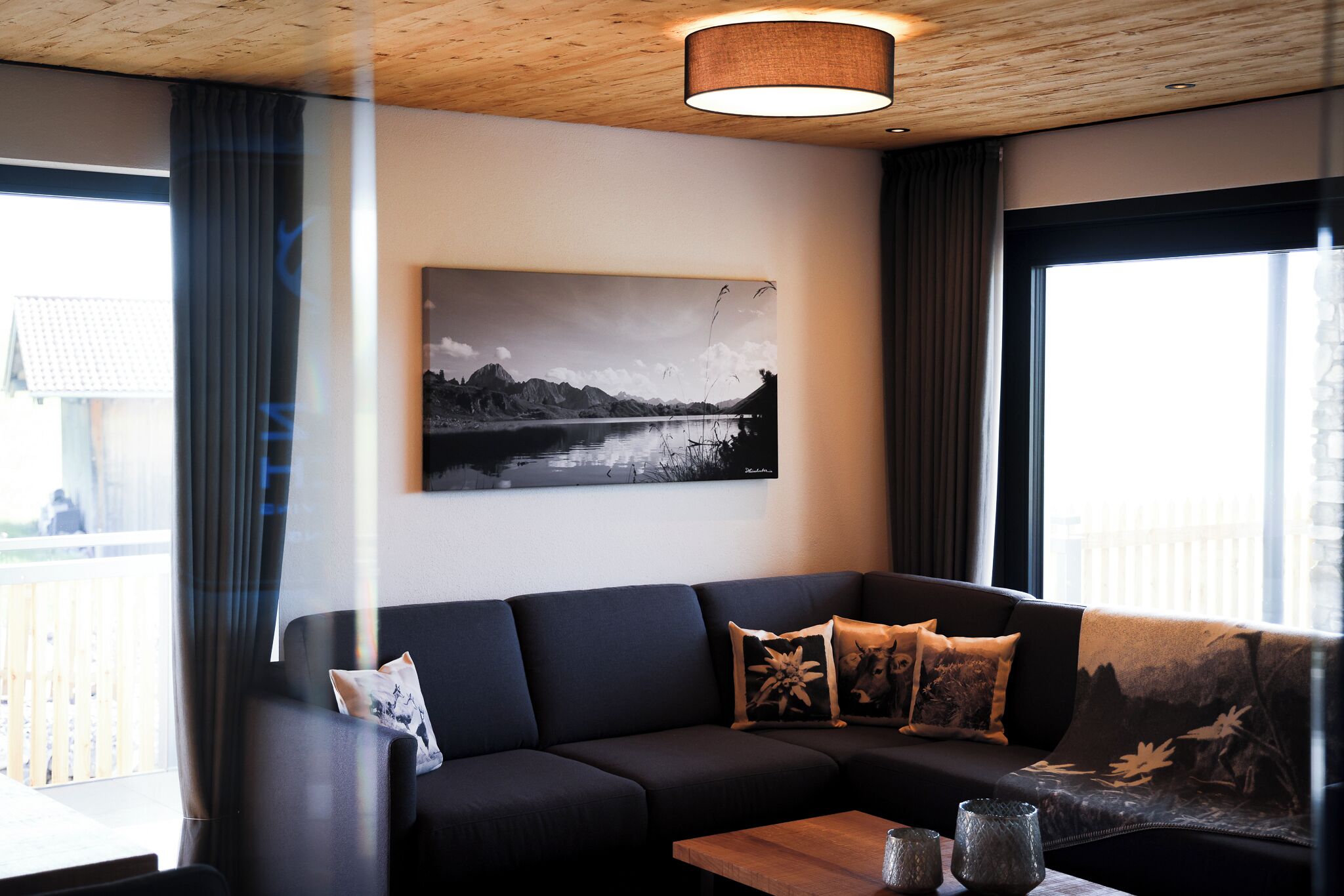 A modern living room with a black sofa, a wooden coffee table, and a large window with curtains.