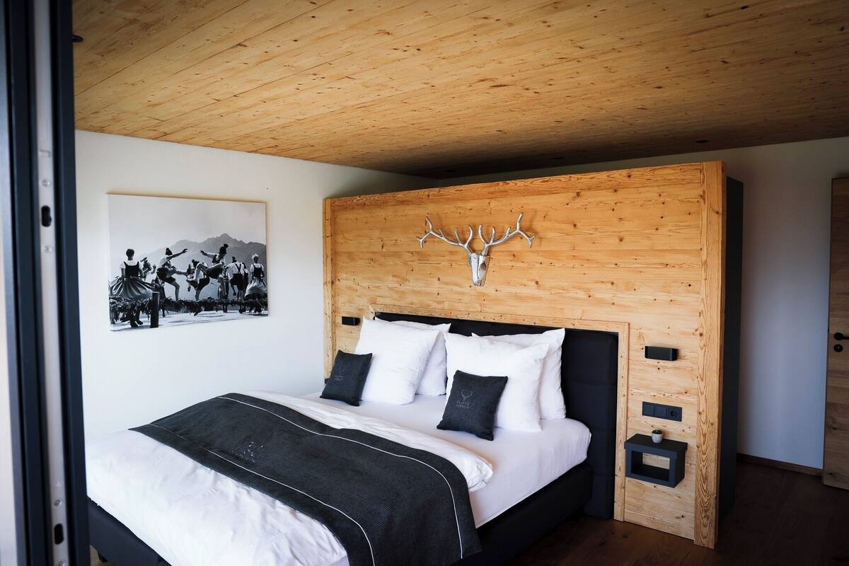 A bedroom with a wooden headboard, a bed with white bedding, two bedside tables, and a wall-mounted artwork.