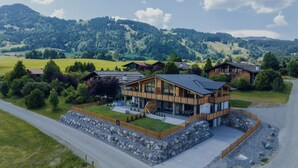 A modern two-story house with a large balcony, surrounded by a stone retaining wall and a well-maintained lawn. - Platzhirsch First Class Living (Ofterschwang)