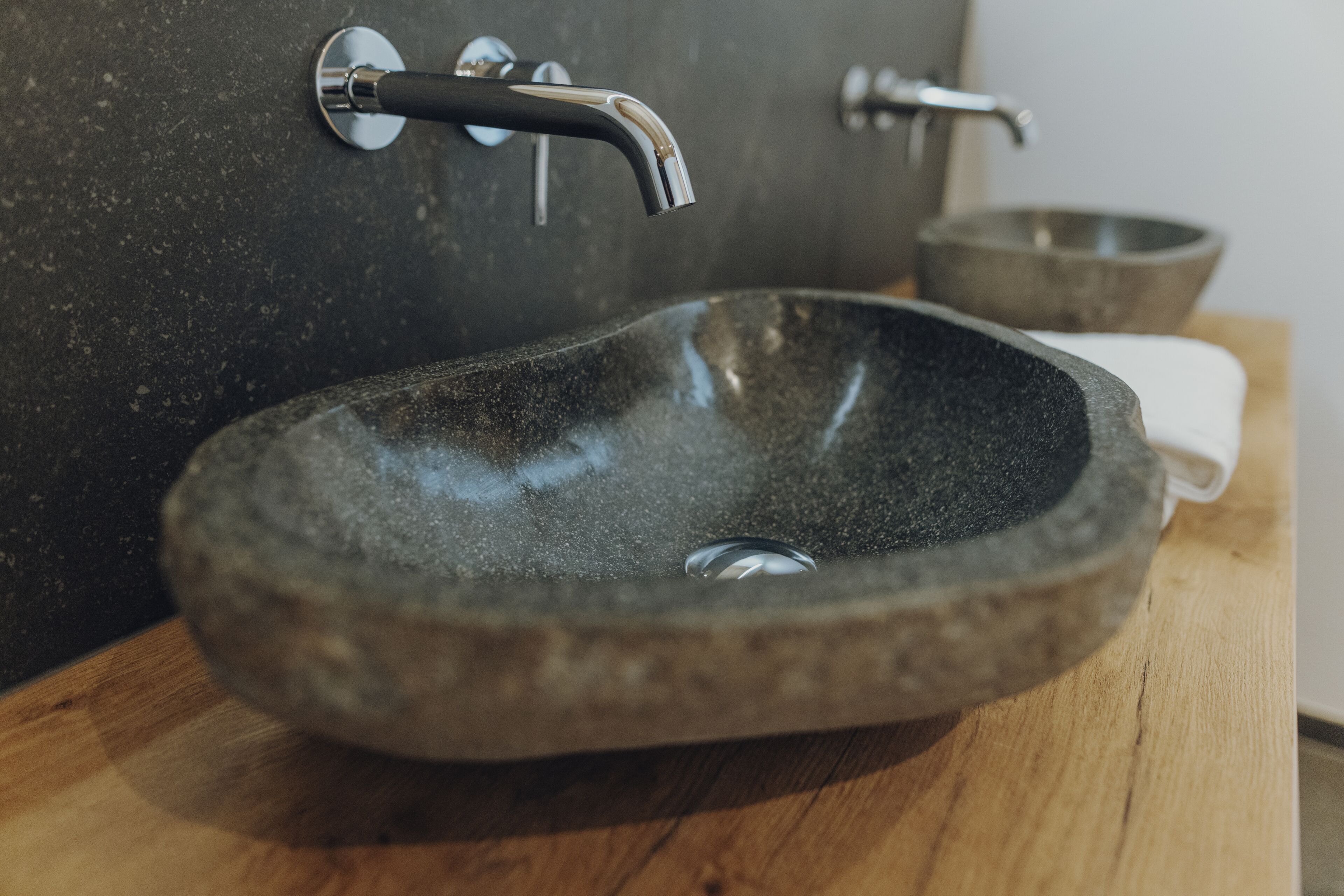 A stone sink with a modern faucet, a wooden countertop, and a stone bowl in the background.