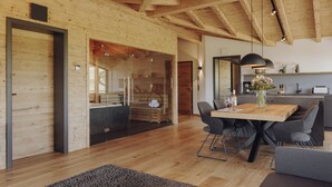 A modern kitchen with wooden beams, a dining area with a wooden table and chairs, and a glass door leading to a living space. - Platzhirsch First Class Living (Ofterschwang)