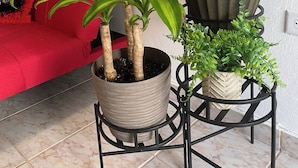 A living room with a red sofa, two potted plants on a black metal stand, and a wall with a motivational poster. - Quiet accommodation 15 minutes away from the airport. Apartment 1 (Trujillo Alto)