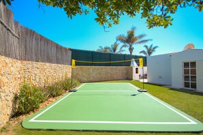 An outdoor netball court with a stone wall, a building with a white exterior, and palm trees in the background. - Stylish Villa w/ Heatable Pool near Galé Beach (Albufeira)