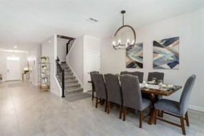 Un espace repas avec un escalier menant à un autre niveau, un lustre et des œuvres d’art abstraites accrochées au mur.