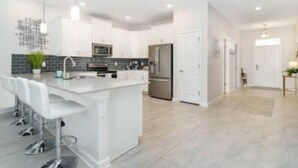 A modern kitchen with white cabinetry, a central island with bar stools, stainless steel appliances, and a black backsplash. - Disney, Orlando, Treehouse, Arcade, Pool, Hot Tub! (Davenport)