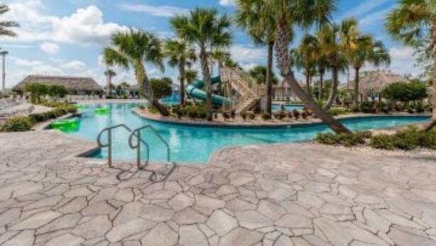 A resort pool area with palm trees, a water slide, and a thatched-roof building. - Disney, Orlando, Treehouse, Arcade, Pool, Hot Tub! (Davenport)