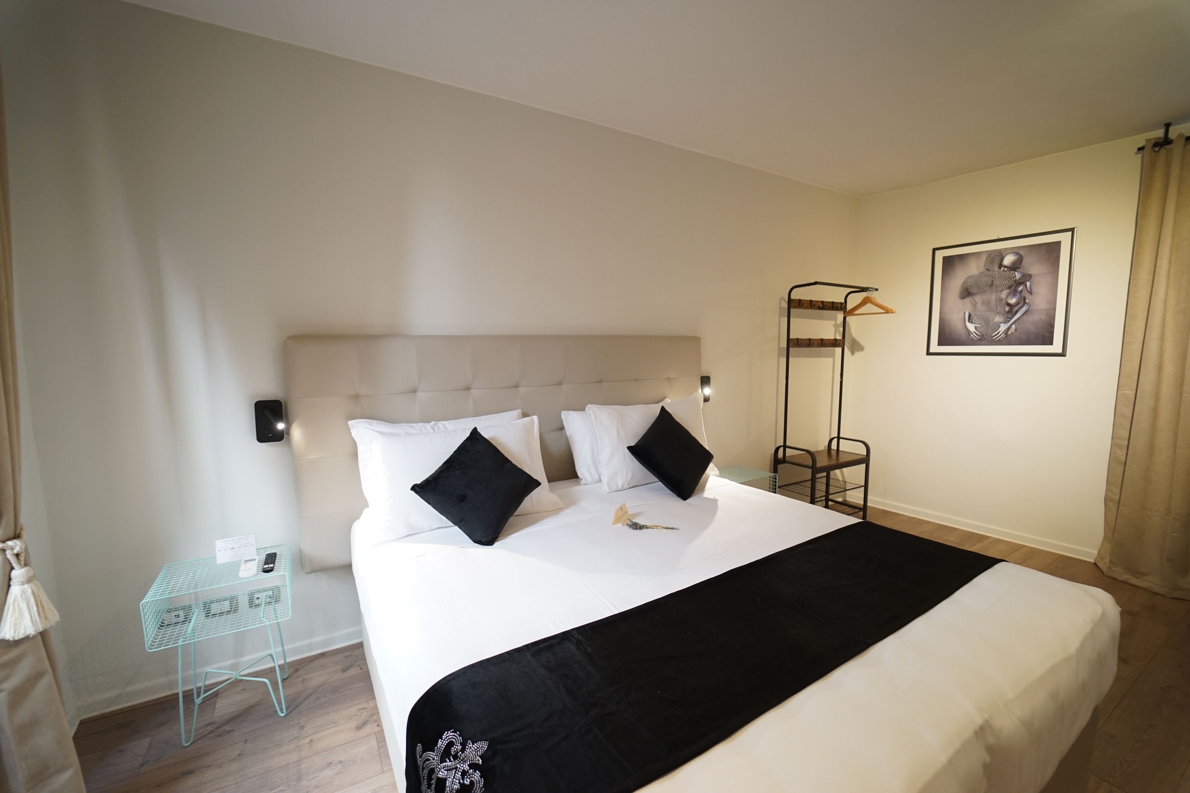A hotel room with a large bed, a bedside table, a chair, and a framed artwork on the wall.