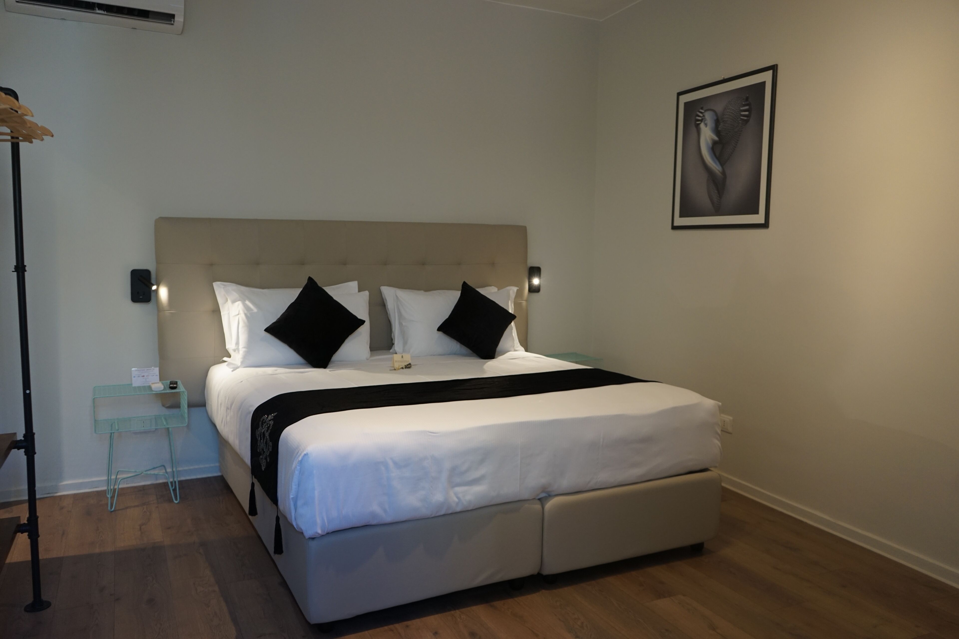 Un dormitorio ordenado con cama, mesitas de noche, una obra de arte en la pared y una lámpara de pie.