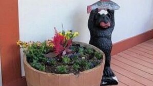 A wooden planter with colorful flowers on a wooden deck, a decorative dog statue, a wall-mounted lantern, and a wreath. - Romantic Little Houses In Mountain, Bedrooms #7 (Brcko)