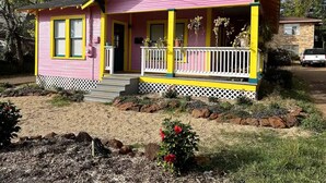 A pink and yellow house with a porch, surrounded by a garden with rocks and plants. - The Big Pink
 (Nacogdoches)