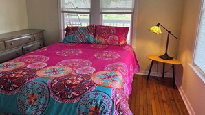 A bedroom with a large bed, two windows with blinds, a bedside lamp, and a dresser. - The Big Pink
 (Nacogdoches)