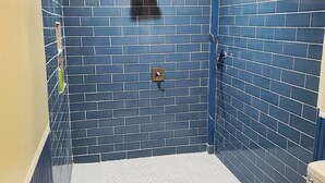 A bathroom with blue and beige tiled walls, a shower with a handheld showerhead, and a toilet. - The Big Pink
 (Nacogdoches)