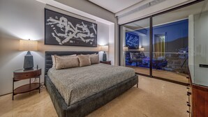 Een moderne slaapkamer met een groot bed, twee nachtkastjes met lampen, een groot abstract schilderij en een schuifglazen deur die leidt naar een balkon met uitzicht op de stad.