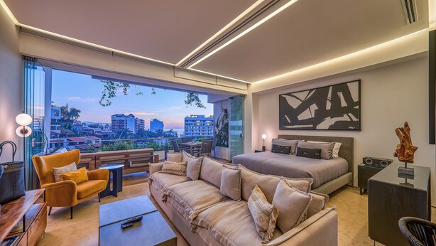 Ein modernes Hotelzimmer mit einem großen Bett, einer Couch, einem Schreibtisch und Blick auf die Stadt.