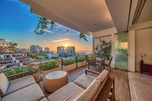 Een modern balkon met uitzicht over de stad, een rond rieten tafeltje en een bank.