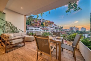 A balcony with a dining setup, including a table and chairs, overlooking a cityscape with colorful buildings.