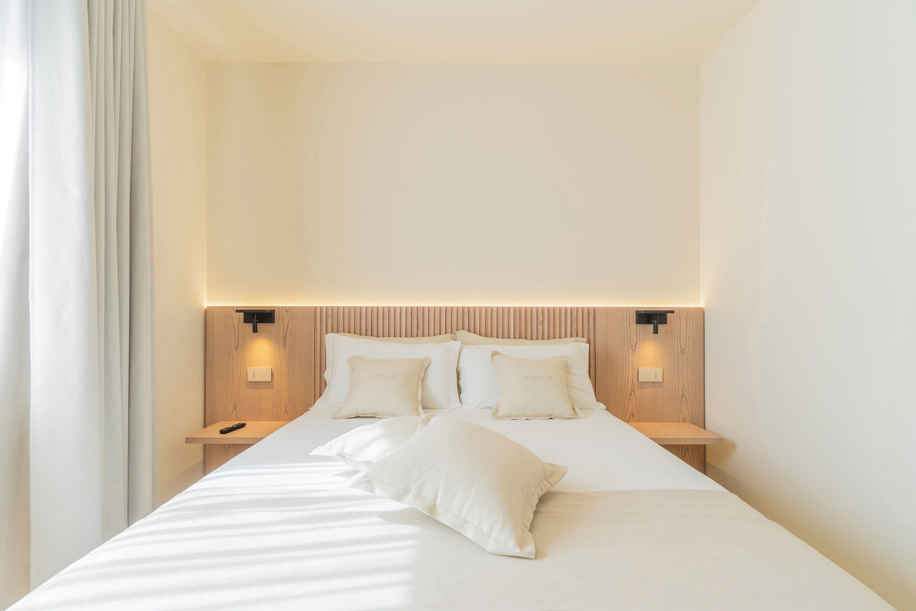 Ein modernes Hotelzimmer mit einem großen Bett, zwei Nachttischen und einem Kopfteil mit integrierter Beleuchtung.