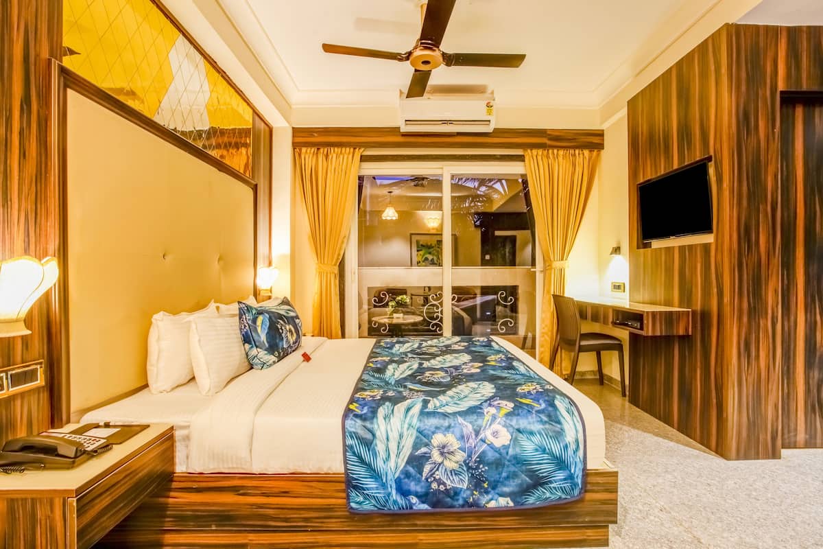 Habitació d'hotel amb llit, escriptori, televisió i balcó amb cortines.